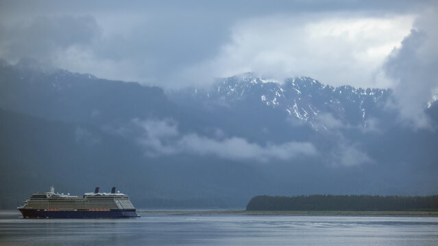 Luxury cruiseship cruise ship liner Solstice sailing the Inside Passage with panoramic mountain range glacier views in Fjord during Alaska Adventure Wilderness cruising with coast line and low clouds
