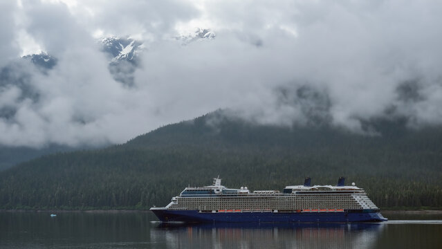 Luxury cruiseship cruise ship liner Solstice sailing the Inside Passage with panoramic mountain range glacier views in Fjord during Alaska Adventure Wilderness cruising with coast line and low clouds