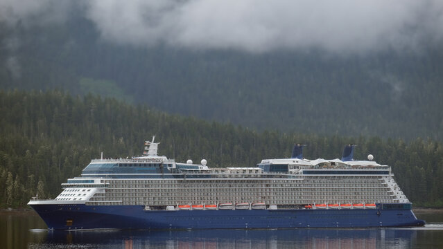 Luxury cruiseship cruise ship liner Solstice sailing the Inside Passage with panoramic mountain range glacier views in Fjord during Alaska Adventure Wilderness cruising with coast line and low clouds