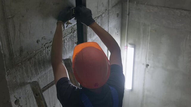 Worker installing elevator guide rail inside concrete lift shaft