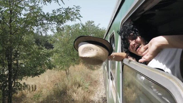 Happy traveler woman wave hands on trip traveling with train and holding a hat in hand. She is looking out the window and she is enjoying the view