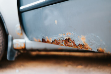 The lower side of a vehicle shows significant rust damage with visible corrosion and peeling paint....