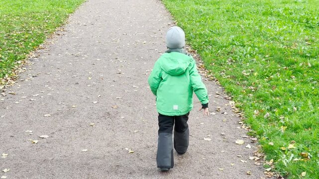 A happy child walks forward holding a paper plane along a leafy park path. The innocent boy enjoys a serene autumn moment in Pushkin, Saint Petersburg in slowmo.