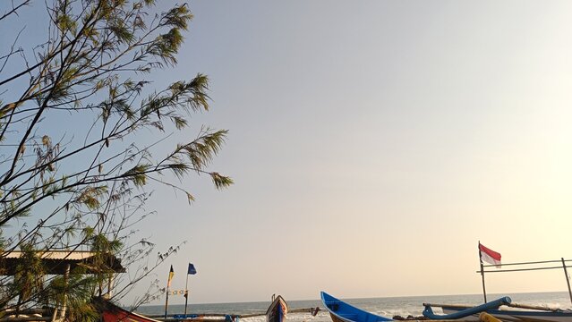 Traditional Indonesian fishing boat with a national flag parked on the coast of Purworejo beach, Central Java under a bright afternoon sky