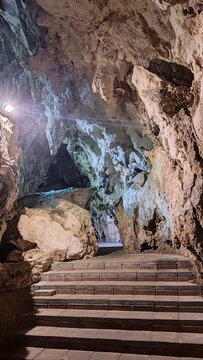 Mystical interior of a limestone cave with concrete stairs lit by artificial spotlight.