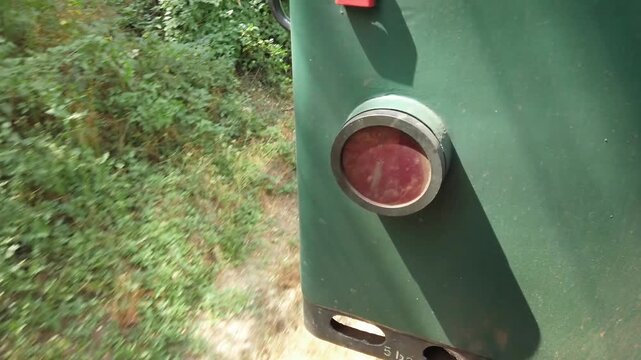 A green train car with a red tail light traveling on track on sunny day