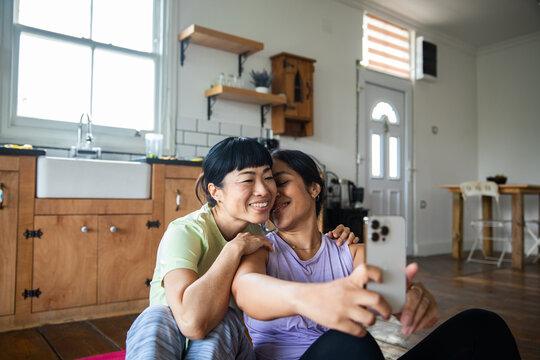 Two women cuddling while taking a selfie in the kitchen