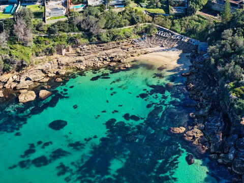 Aerial view of Gordons Bay featuring turquoise waters, rocky shoreline, and small boats pulled up on the sandy beach in Coogee, New South Wales, Australia.