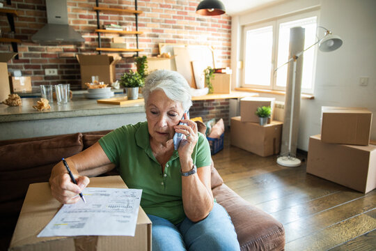 Senior woman on phone reviewing moving paperwork at home