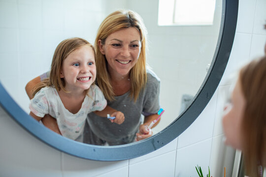 Mother and daughter brushing teeth and smiling in mirror