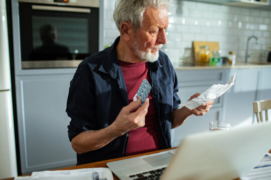 Senior man reading medication leaflet at kitchen table