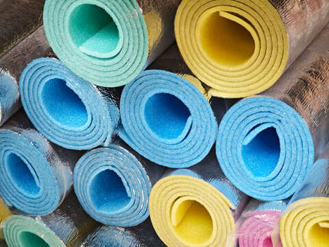 Rolls of foil backed foam insulation stacked, colorful blue yellow green pink spiral cross sections, thermal underlay material for construction renovation, top view from above