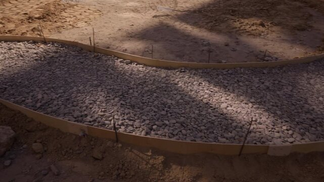 Gravel base prepared inside curved formwork for concrete pathway