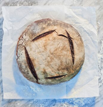 Sourdough bread loaf dusted with flour on marble slab