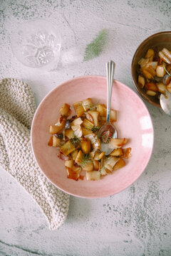 Leek confit dish garnished with fennel herb in pink bowl
