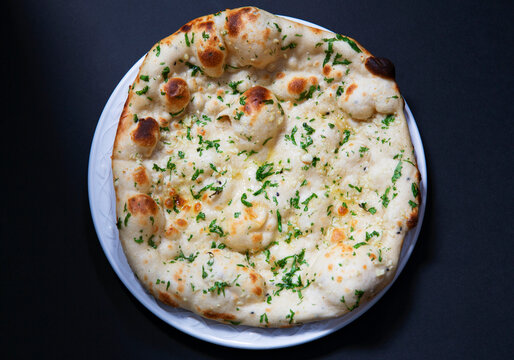 Indian naan bread with garlic and herbs on white plate