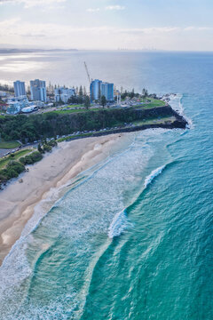 Aerial view of Duranbah Beach with turquoise waves breaking on the sand, coastal buildings, a construction crane, and green parkland in Duranbah, New South Wales, Australia.