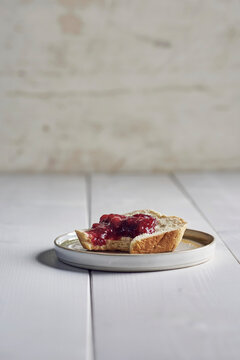 Bitten slice of brioche bread with butter and jam on a white plate