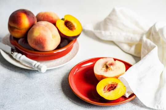 Ripe peaches halved and whole in fruit bowl and red plate
