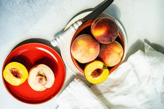 Peaches in a brown bowl with cut halves on a red plate