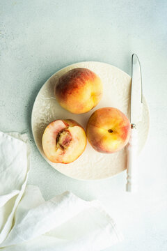 Three Peaches on a white ceramic plate with a serrated knife