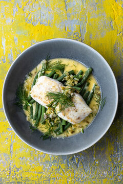 Hake with green beans and butter sauce in a gray bowl