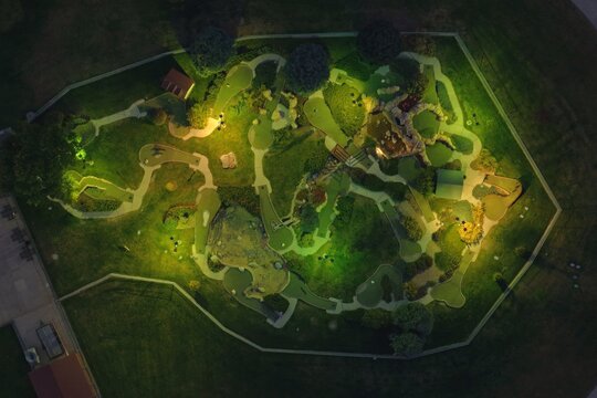 Aerial view of a mini-golf course at night, illuminated by artificial lights, featuring winding paths, putting greens, and landscaping in Greeley, Colorado, United States.