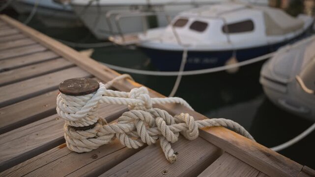 Mooring line tied in a secure knot on a wooden harbor pier. Concept of nautical safety, boat anchoring, maritime travel, and peaceful marina life. 4K.