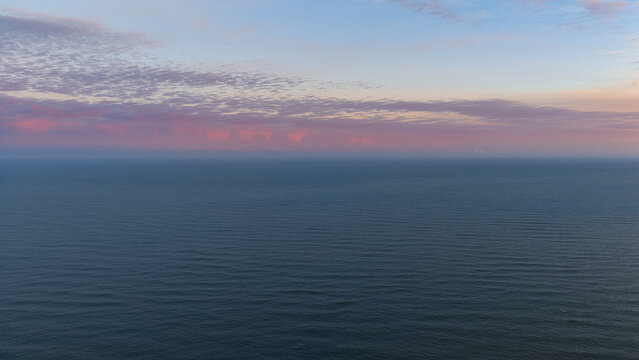 Aerial view of the calm ocean under a soft pink sunset sky off the coast of Eyrarbakki, Sveitarfelagid Arborg, Iceland.