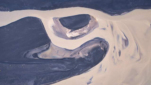 Aerial view of braided glacial river channels with dark volcanic sand and light-colored sediment creating intricate patterns in Eyrarbakki, Sveitarfelagid Arborg, Iceland.