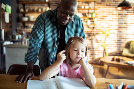 Man helping bored girl with homework at kitchen table
