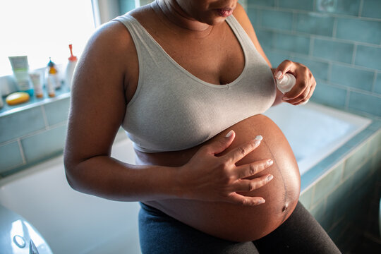 Pregnant woman applying belly lotion in bathroom