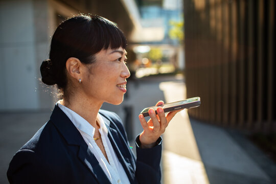 Businesswoman using voice assistant on smartphone outdoors