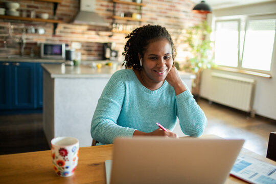Smiling woman on laptop video call taking notes at home
