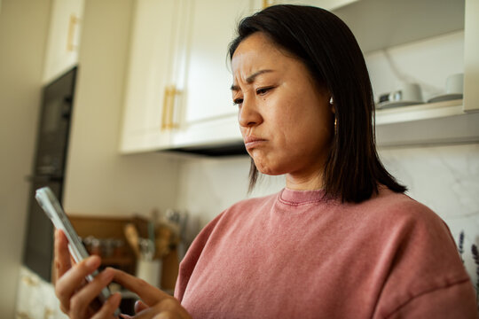 Woman frowning at smartphone in home kitchen