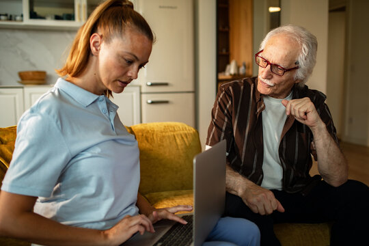 Young woman teaching senior man on a laptop at home