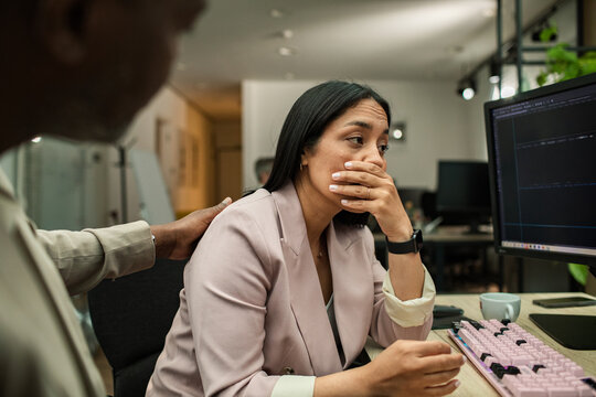 Coworker comforting stressed woman at office computer