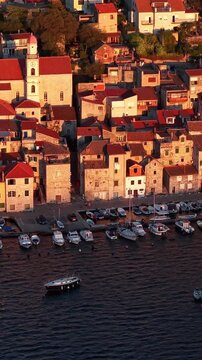 Croatia, aerial view of Sibenik historic old town with stone houses, red roofs, church tower, and boats moored in the harbor at sunset