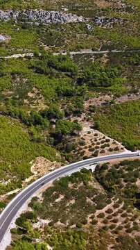 Croatia, aerial view of a winding road through a mountainous landscape with green trees and a driving car, footage