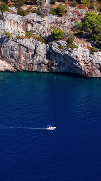 Croatia, aerial view of a small boat moving on the blue sea along the rocky cliff coast