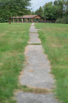 Distant park pavillion and picnic tables at the end of a long narrow paved path thru the grass
