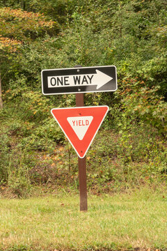 on a wooden post sit two road signs one on top of each other, a one way street arrow and a yield triangle to help guide traffic flow
