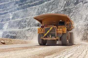 A giant dump truck follows a haul road through an open-pit mine in Chile, with dust around its wheels and exposed rock benches emphasizing the scale of the extraction site. © Jose Luis Stephens