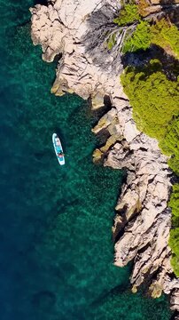 Croatia, aerial view of a person paddleboarding in clear turquoise sea water near rocky coast with pine trees