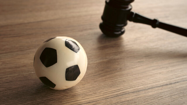Miniature soccer ball next to judge gavel on wooden desk concept of sports law regulation disciplinary hearing contract match fixing and legal arbitration