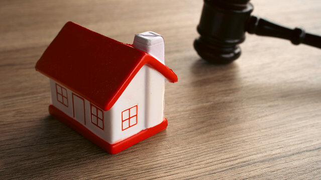 Small model house positioned beside judge gavel on wooden surface concept of real estate law mortgage foreclosure property rights eviction and auction judgment