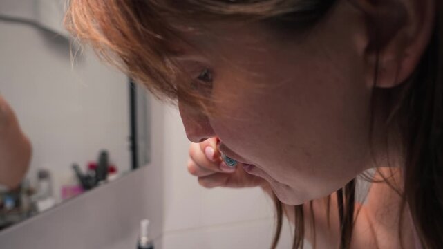 Close up of a woman brushing her teeth and spitting blood into a bathroom sink, showing possible gum bleeding during oral hygiene. High quality 4k footage