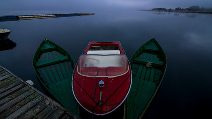 Red and green wooden boats moored at dock in calm dawn lake © A
