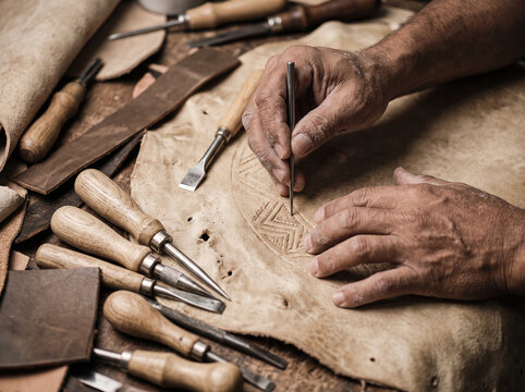 Artisan leather crafter tooling an intricate geometric pattern on genuine leather using traditional hand tools in a workshop