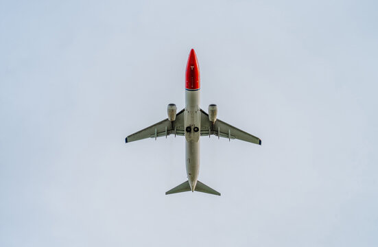Passenger aircraft flying overhead, photographed from directly beneath the fuselage with wings and engines clearly visible against a pale blue sky. Strong symmetrical composition suitable for travel, 